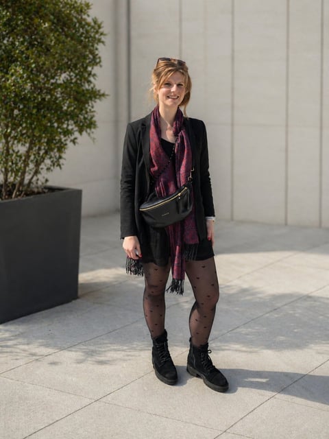 Frau in schwarzer Strickjacke, burgunder Schal und schwarzen Stiefeln, im Freien vor modernem weißem Hintergrund